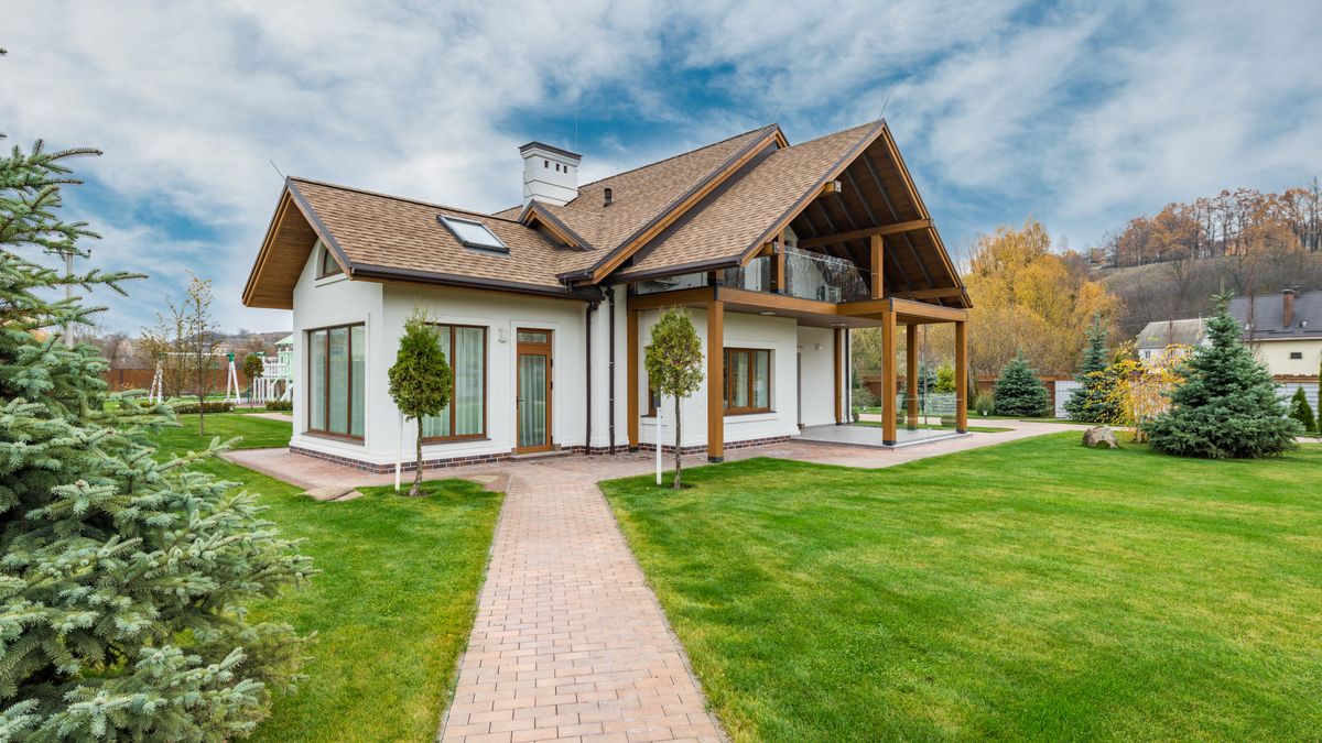 Modern cottage-style house with a green lawn and trees under a blue sky
