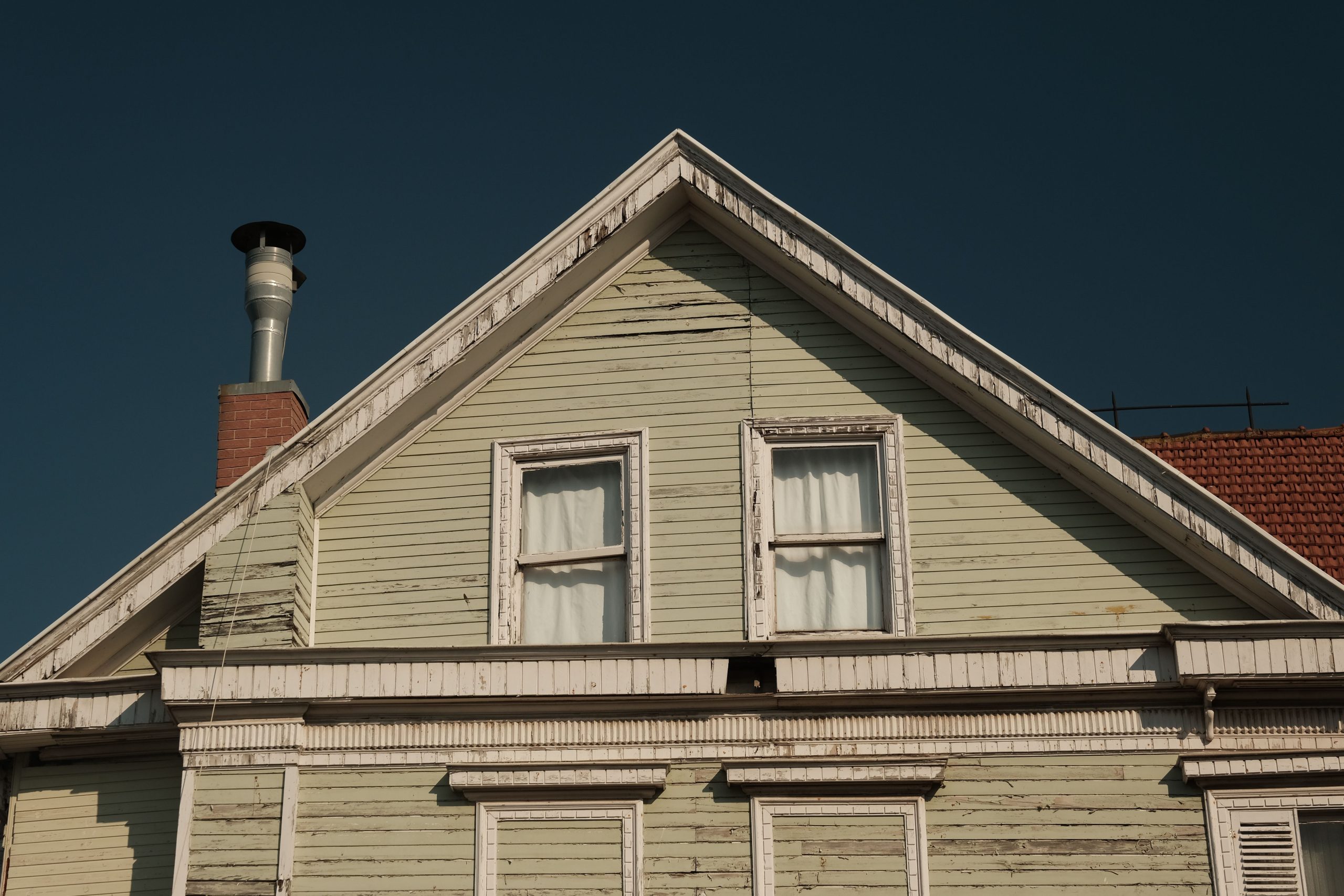 Close-up of a weathered wooden house facade with a brick chimney against a clear sky