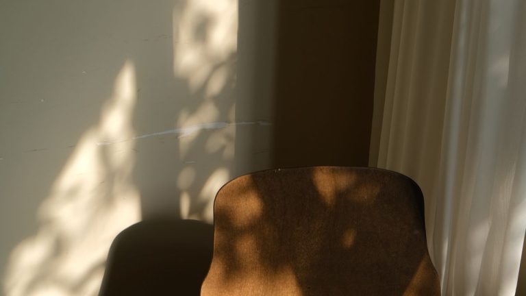 Wooden chair in a sunlit empty room casting long shadows on the wall