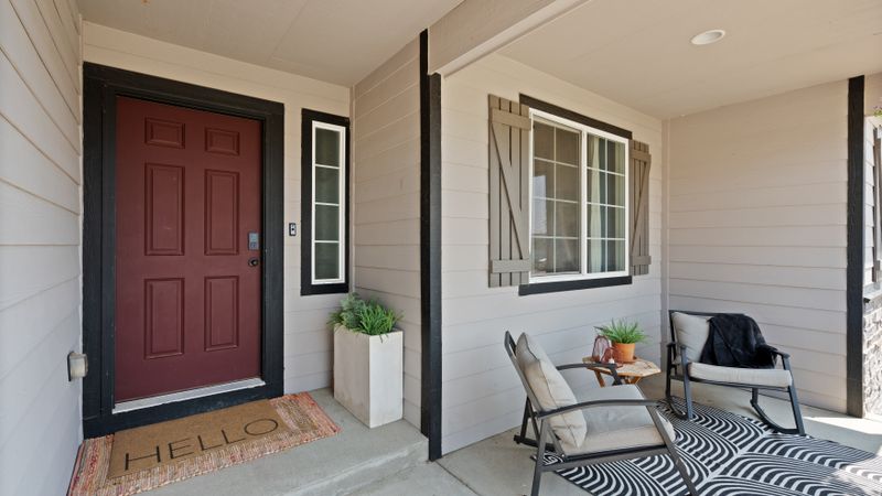 Front porch with two cushioned chairs, a doormat and potted plants beside the door