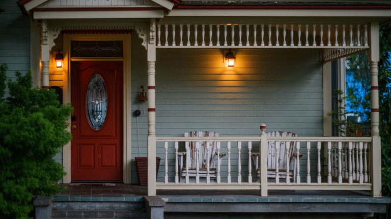 Front porch with a red door, wooden armchairs and warm porch lights in the evening