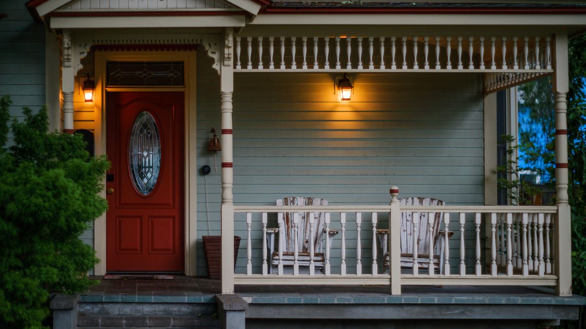 Front porch with a red door, wooden armchairs and warm porch lights in the evening