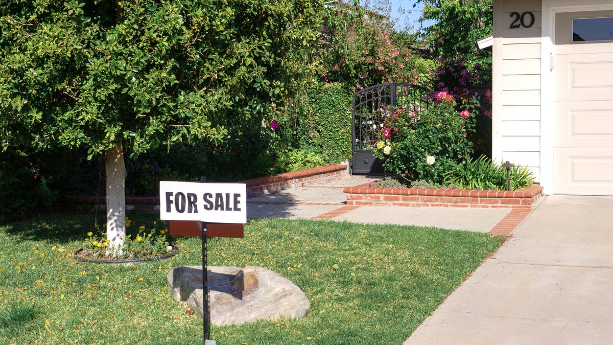 Front view of a house with a garden and a for sale sign on the lawn