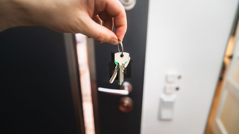 Hand holding house keys in front of an open door of a new home