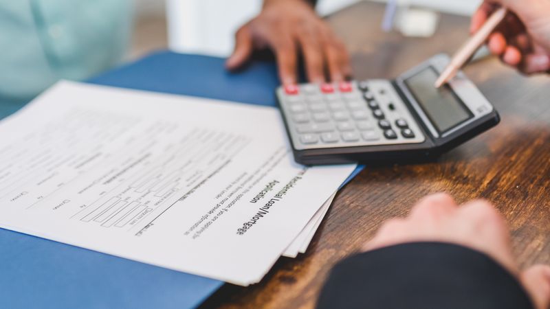 Hands using a calculator beside real estate documents on a desk