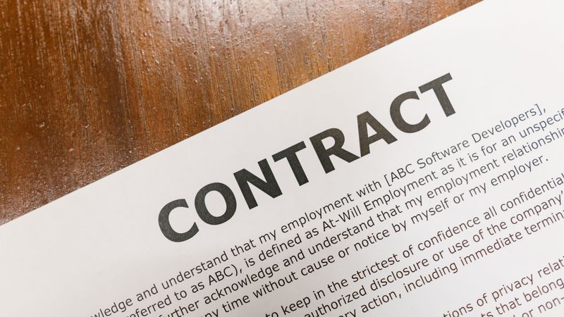 A printed contract document lying on a dark wooden table