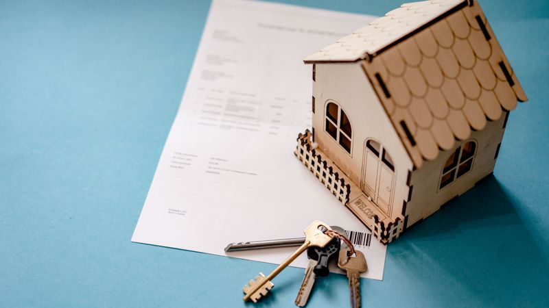 Miniature wooden house beside house keys and a contract on a table