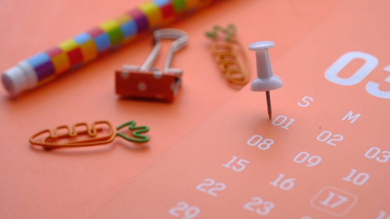 White push pin on an orange desk calendar page next to office supplies