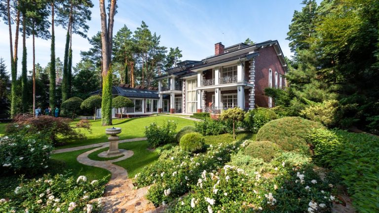 House exterior with a garden path, green lawn and trees under a blue sky